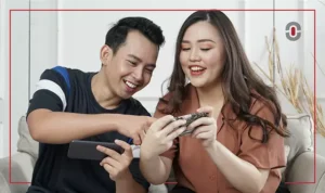 A smiling young Filipino man and woman sitting together on a couch, engaged in an interactive experience on a smartphone.