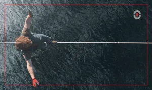 A person wearing gloves and outdoor gear carefully balances on a tightrope above a body of water, symbolizing the challenge of navigating localization complexities.