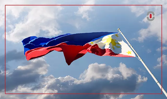 The Philippine flag waves in the wind against a bright blue sky with clouds, representing national identity, cultural pride, and the significance of accurate Filipino translation in preserving language and heritage.