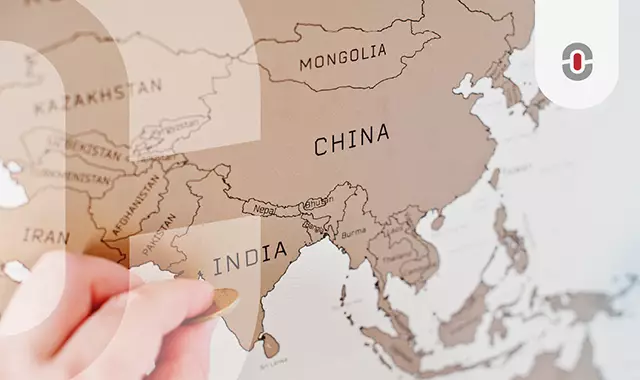 A close-up of a hand using a coin to scratch off a travel map, revealing countries in Asia, representing market expansion and the importance of localization in diverse regions.