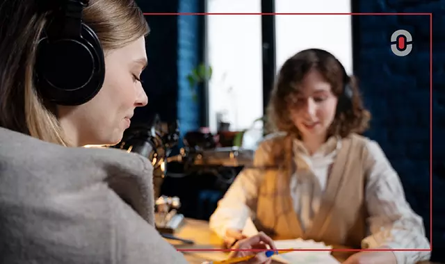 Two women engaged in a podcast recording session, both wearing headphones and speaking into professional microphones. The setting conveys discussion, real-time communication, and the role of technology in enhancing language services.