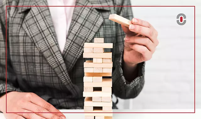 A person in a checkered blazer carefully placing a wooden block on top of a Jenga-style tower, symbolizing the structured approach needed to build an optimal AI translation stack with various integrated components.