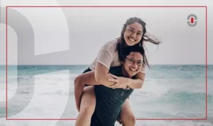 A smiling young Filipino woman playfully giving a piggyback ride to a man at the beach, with the ocean waves in the background. The image conveys joy, warmth, and connection, representing the lively and friendly nature of Filipino culture.