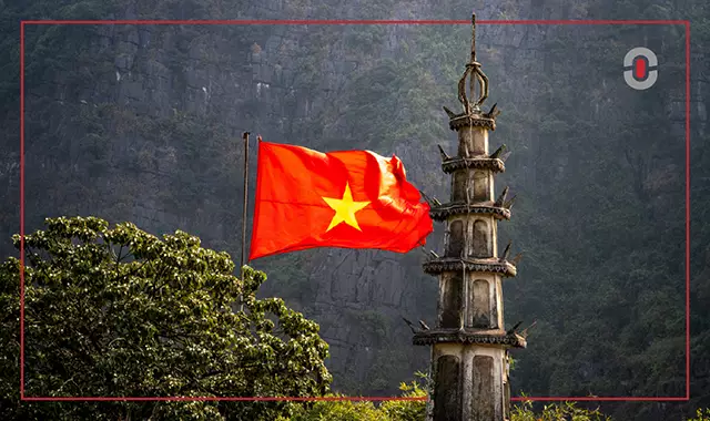 Vietnamese national flag waving beside a traditional stone pagoda set against a mountainous backdrop, symbolizing the country’s cultural and regional identity.